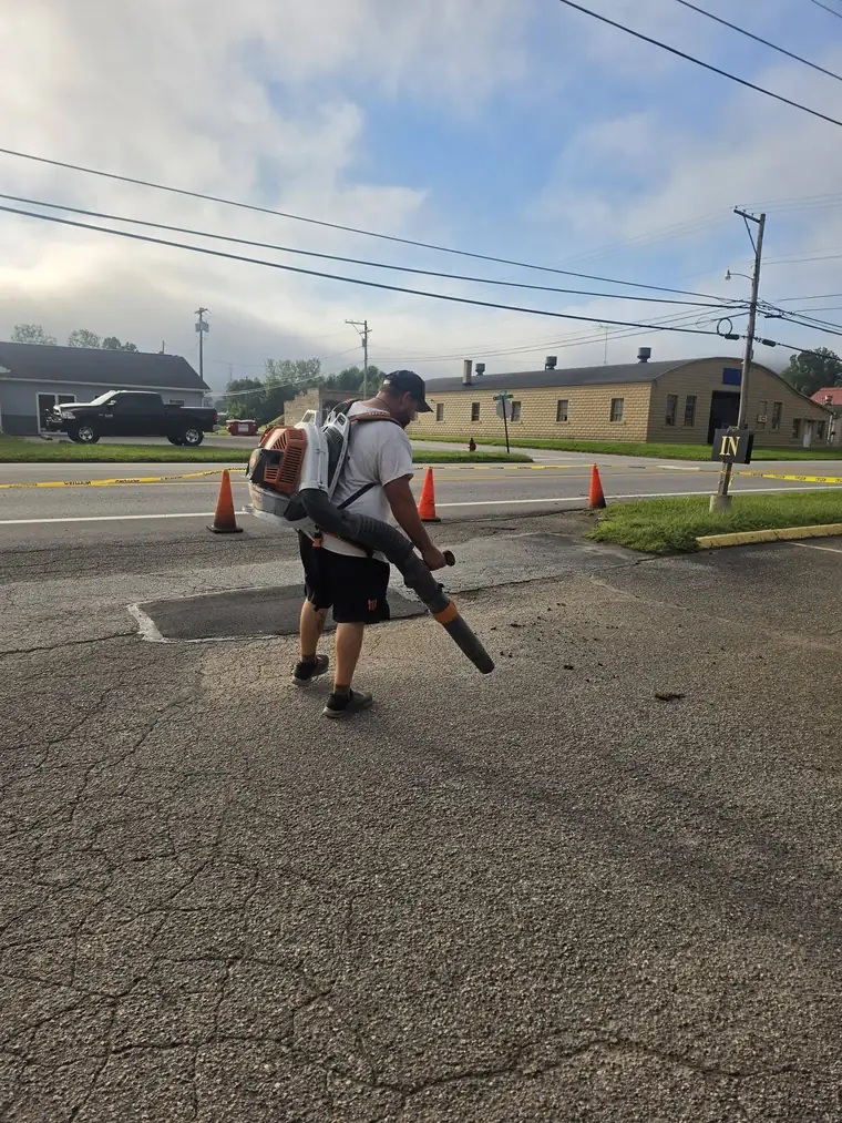 Crew member blowing debris off a parking lot before sealing, New Martinsville area